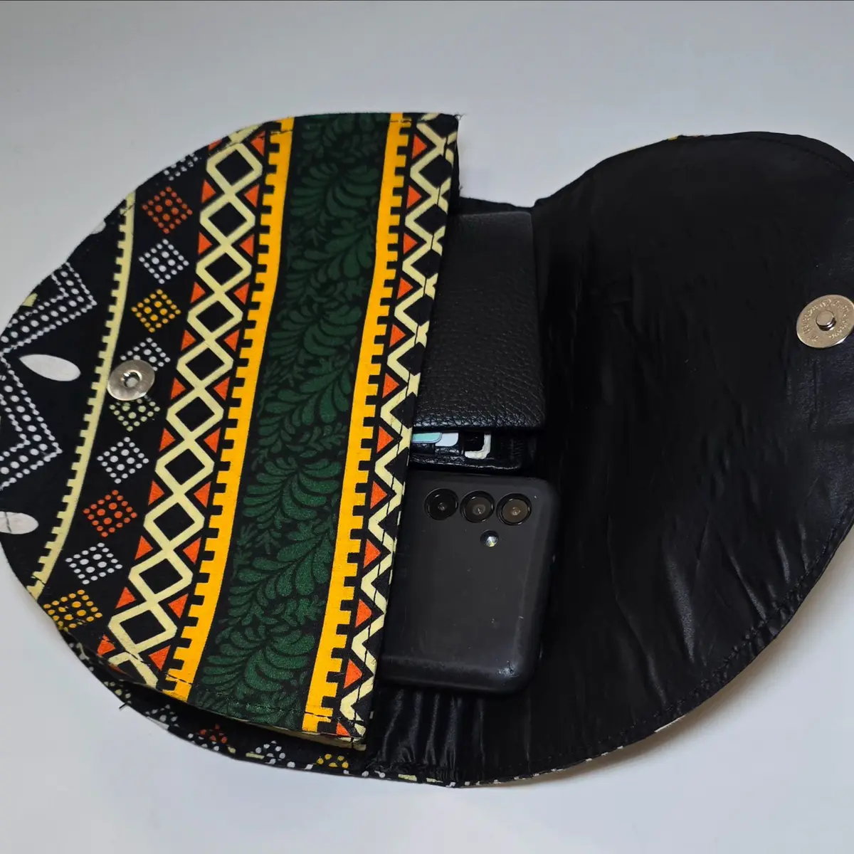 Ankara-patterned clutch bag opened to reveal a spacious interior, showing a phone and other items inside, with a black leather lining and magnetic clasp.
