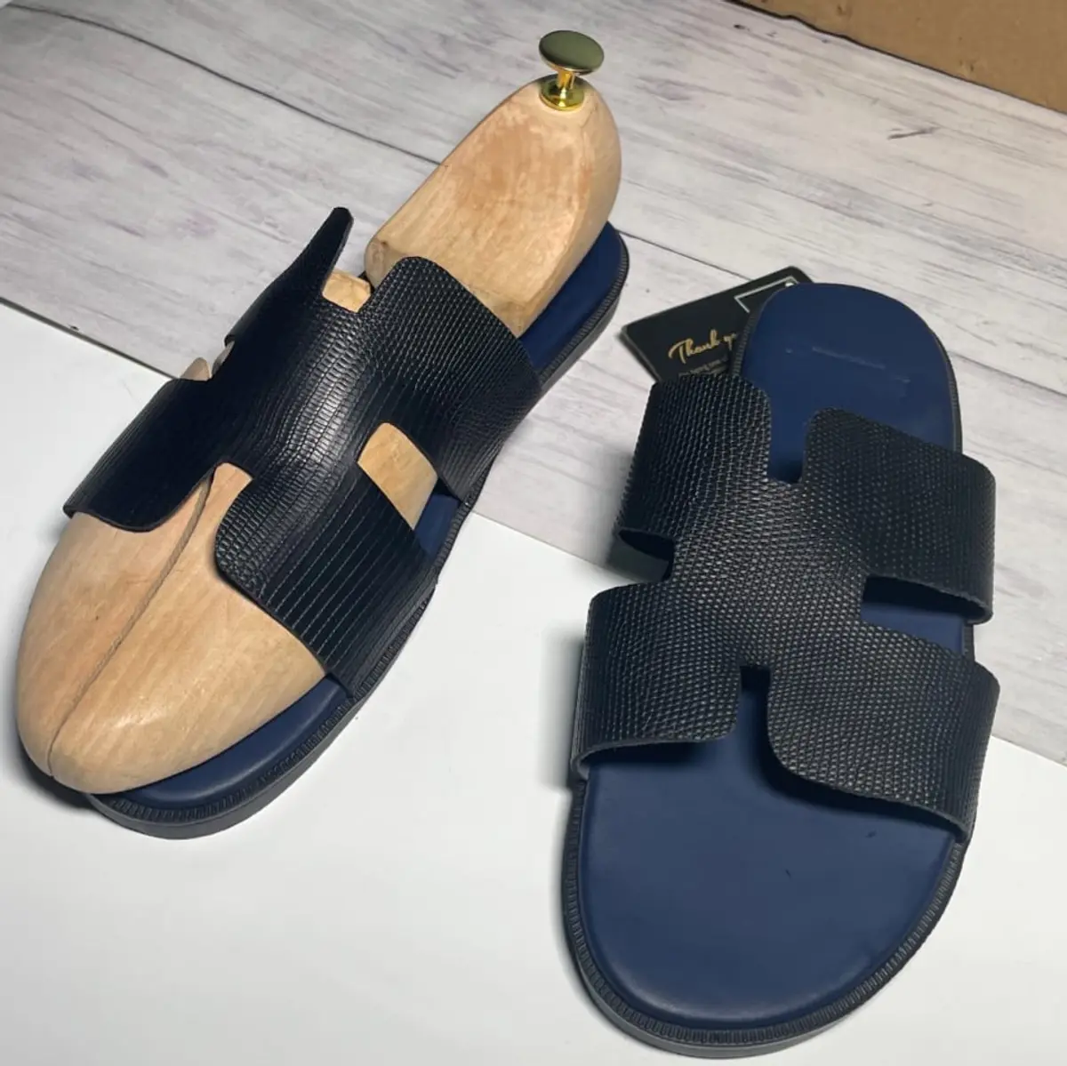 Image of a pair of leather black slippers with a mannequin foot inserted.