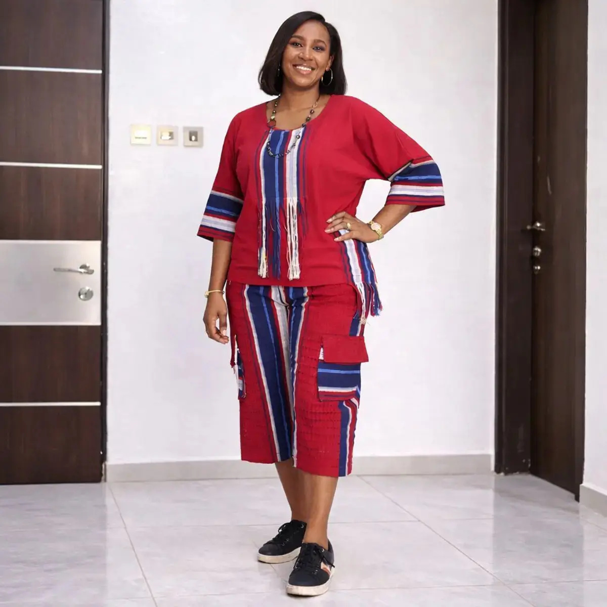 Red and navy striped Aso Oke two-piece women’s outfit featuring fringe-detail top and matching knee-length pants.
