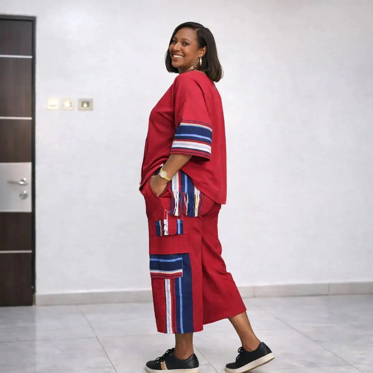 Red and navy striped Aso Oke two-piece women’s outfit featuring fringe-detail top and matching knee-length pants.
