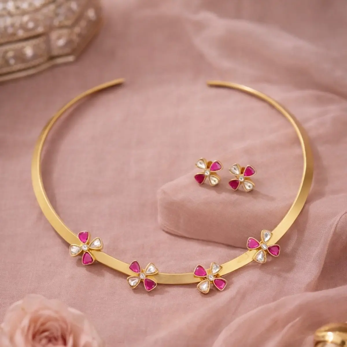 Handcrafted gold floral choker necklace with pink and white gemstone details and matching earrings displayed on blush pink fabric with rose accents, elegant artisan jewelry set.