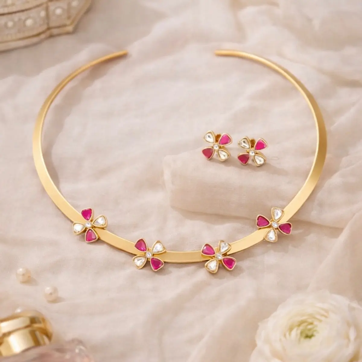 Elegant handmade gold choker necklace with pink and white floral gemstones and matching earrings styled on soft cream fabric, premium artisan statement jewelry.