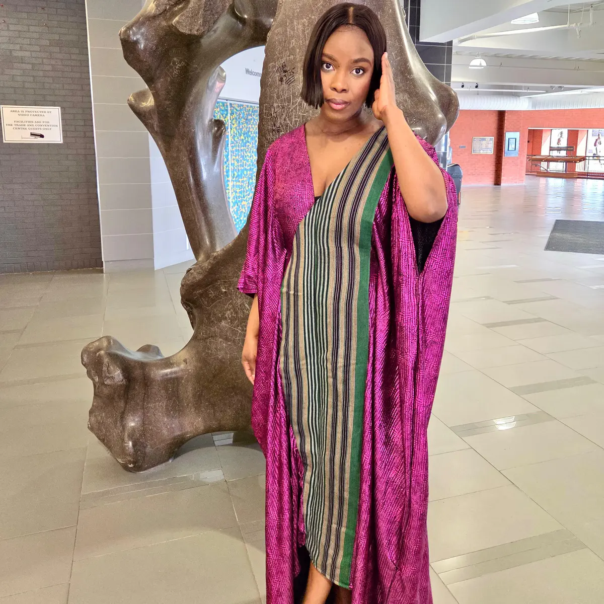 Handcrafted African kaftan dress on female model, showing full-length metallic  fuchsia batwing silhouette with hand-woven green, gold, black and cream stripe  centre panel, deep V-neckline, dramatic floor-sweeping sleeves.  Color: Fuchsia & Green (Metallic with Woven Stripe Panel).