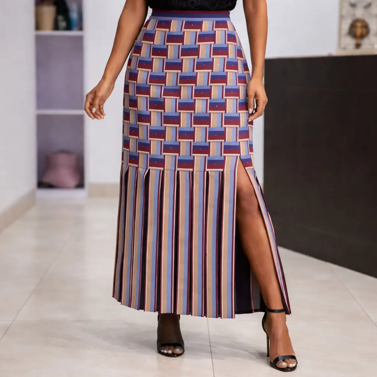 High-waisted Ankara midi skirt with geometric basketweave print in purple, beige, and blue, featuring a front slit and striped hem detail, styled with heels