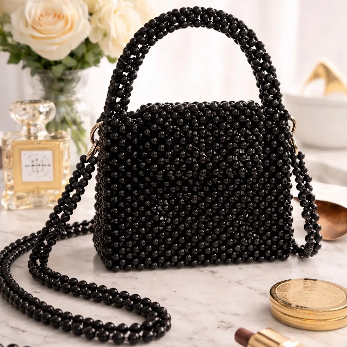 Black beaded mini handbag with top handle and crossbody strap, displayed on marble surface with luxury accessories