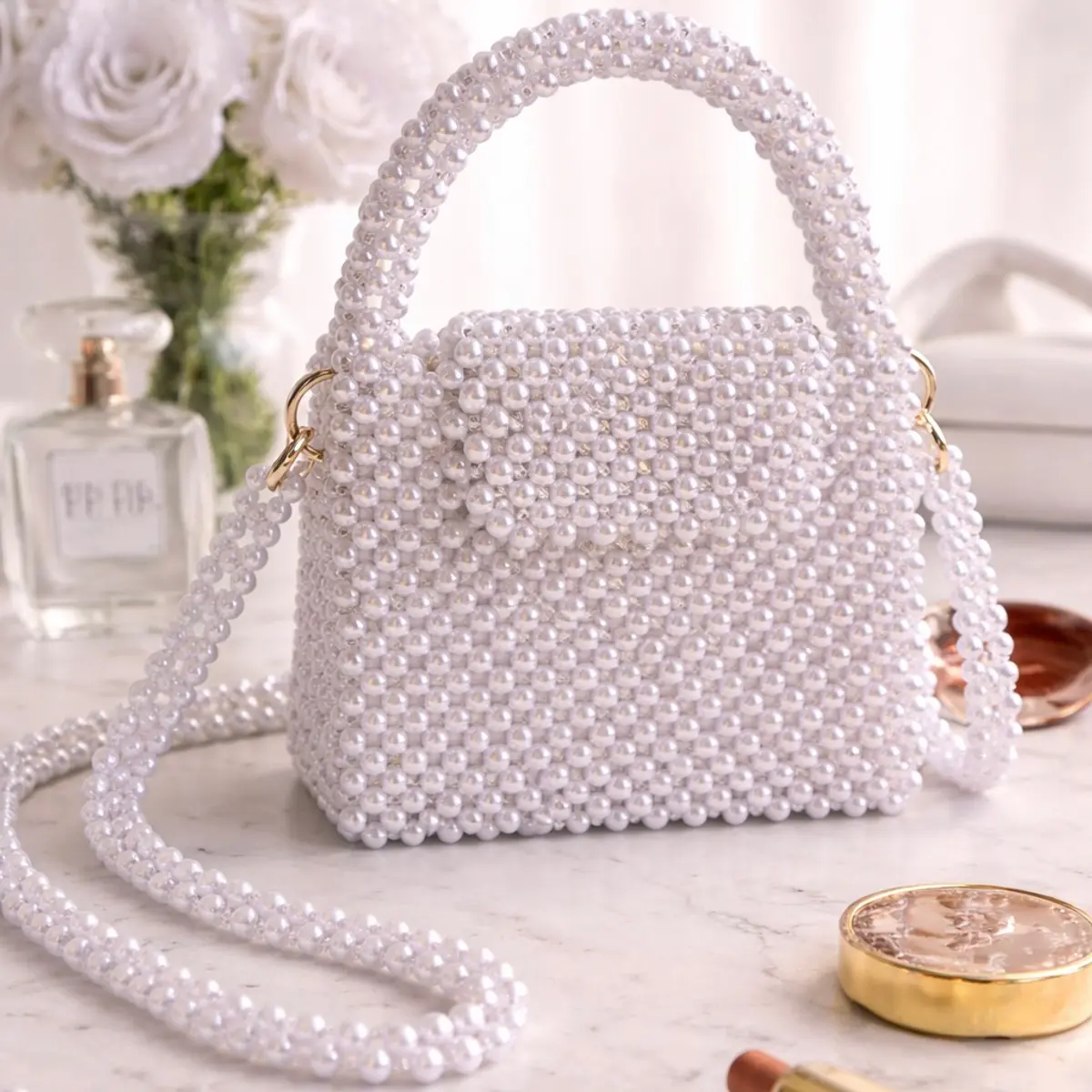 White pearl beaded mini handbag with top handle and crossbody strap, styled on marble surface with perfume and flowers