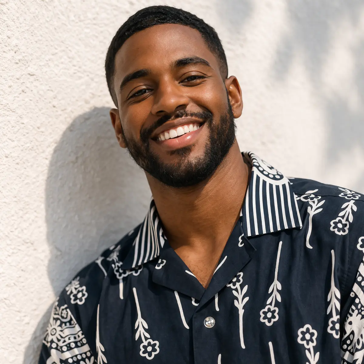 Close-up portrait of a smiling man showcasing the artisan-made shirt's contrast stripe camp collar detail in navy and white, with the hand-embossed-inspired floral and paisley print clearly visible across the chest and shoulder in deep navy blue and crisp white. Color: Navy Blue and White