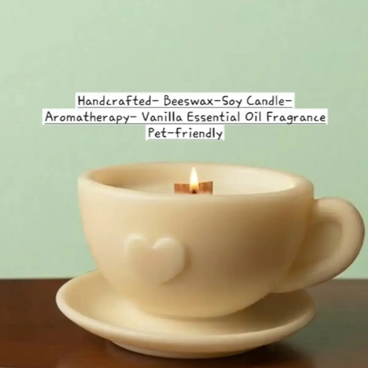 Studio product photograph of a single handcrafted beeswax and soy cup-and-saucer candle shaped like a teacup with a heart embossed on its side, featuring a lit wooden wick and a smooth, warm ivory finish, displayed against a soft sage-green background. Color: Ivory, Warm Cream