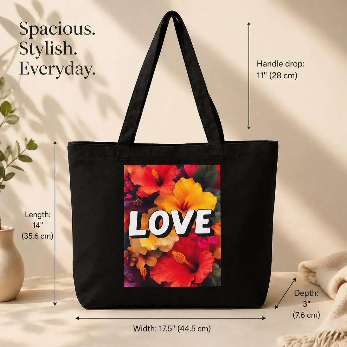 A flat product shot of a spacious black canvas tote bag with dimension annotations showing 17.5 inch width, 14 inch length, 3 inch depth, and 11 inch handle drop. The front panel displays a vibrant hibiscus bouquet print in fiery red, orange, and gold tones with bold white LOVE text. Color: Black