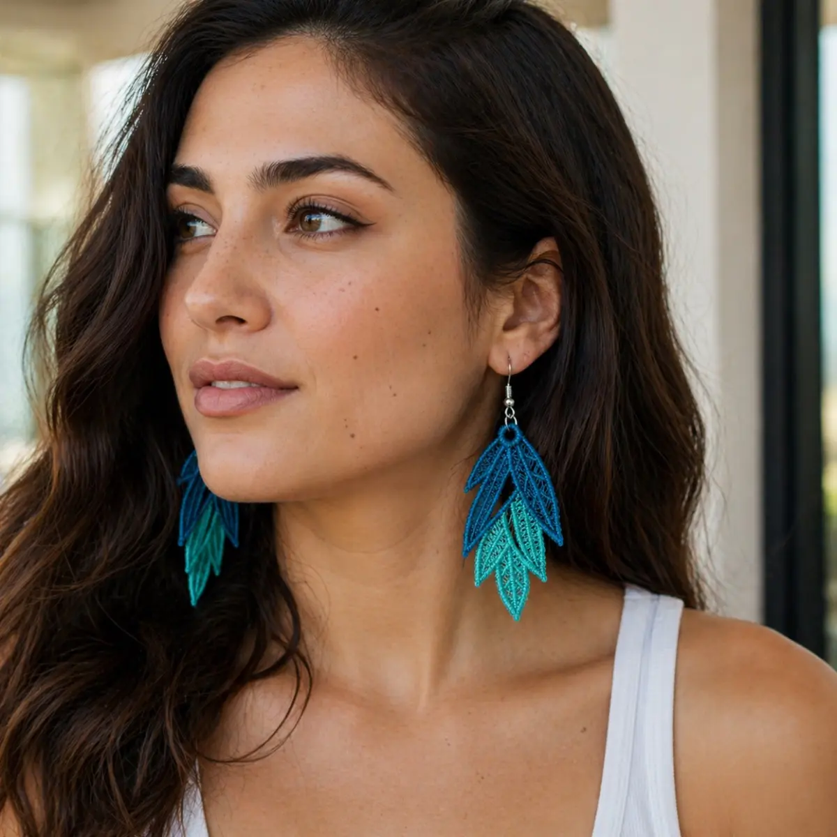 A woman models handcrafted leaf-shaped drop earrings featuring intricate lace-like filigree detailing and a stunning ombre gradient transitioning from deep ocean blue at the top to soft turquoise at the tips. The artisan-made earrings measure 5.5 cm × 2.5 cm and hang from silver-tone fish hook clasps, showcasing delicate layered leaf forms reminiscent of sea and sky. Their lightweight, finely textured construction highlights skilled handmade craftsmanship perfect for bohemian and coastal-inspired styles. Color: Blue, Turquoise